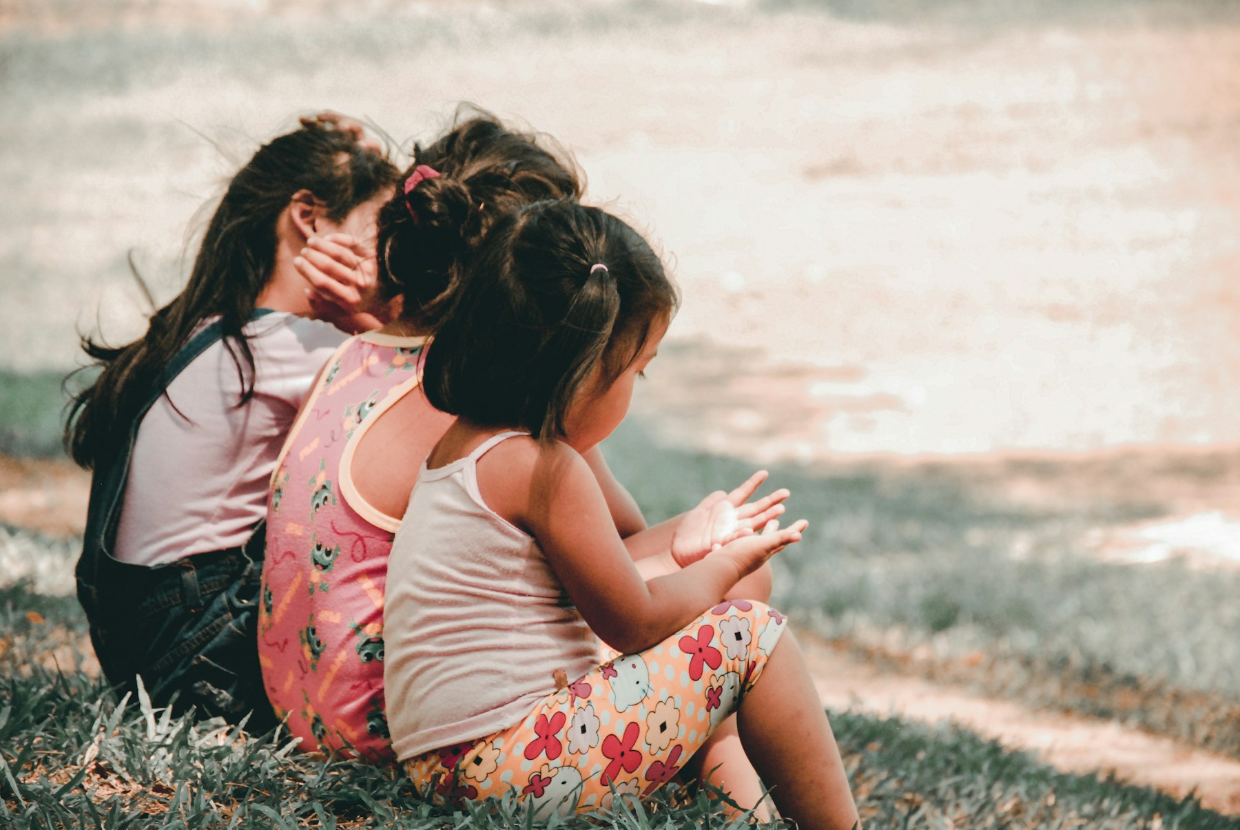 Three young children sitting together outdoors in the grass